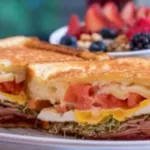A sandwich with layers of ham, egg, cheese, tomato, and lettuce, served on toasted bread