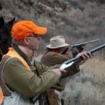 Hunters aiming rifles in wilderness.