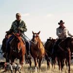 Two hunters riding horses outdoors.